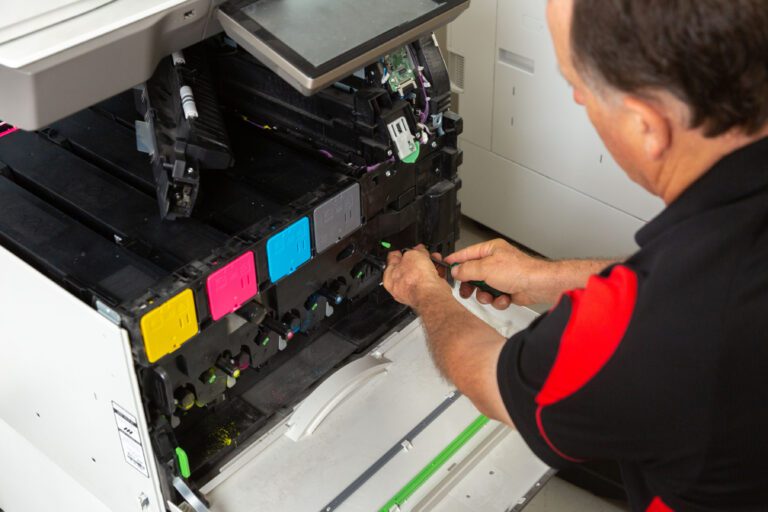 technician opening the front of a photocopier with the toners and working on it with a screwdriver